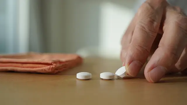 На столе лежат белые таблетки, рука тянется к ним